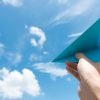Hand launching paper plane toward cloudy blue sky